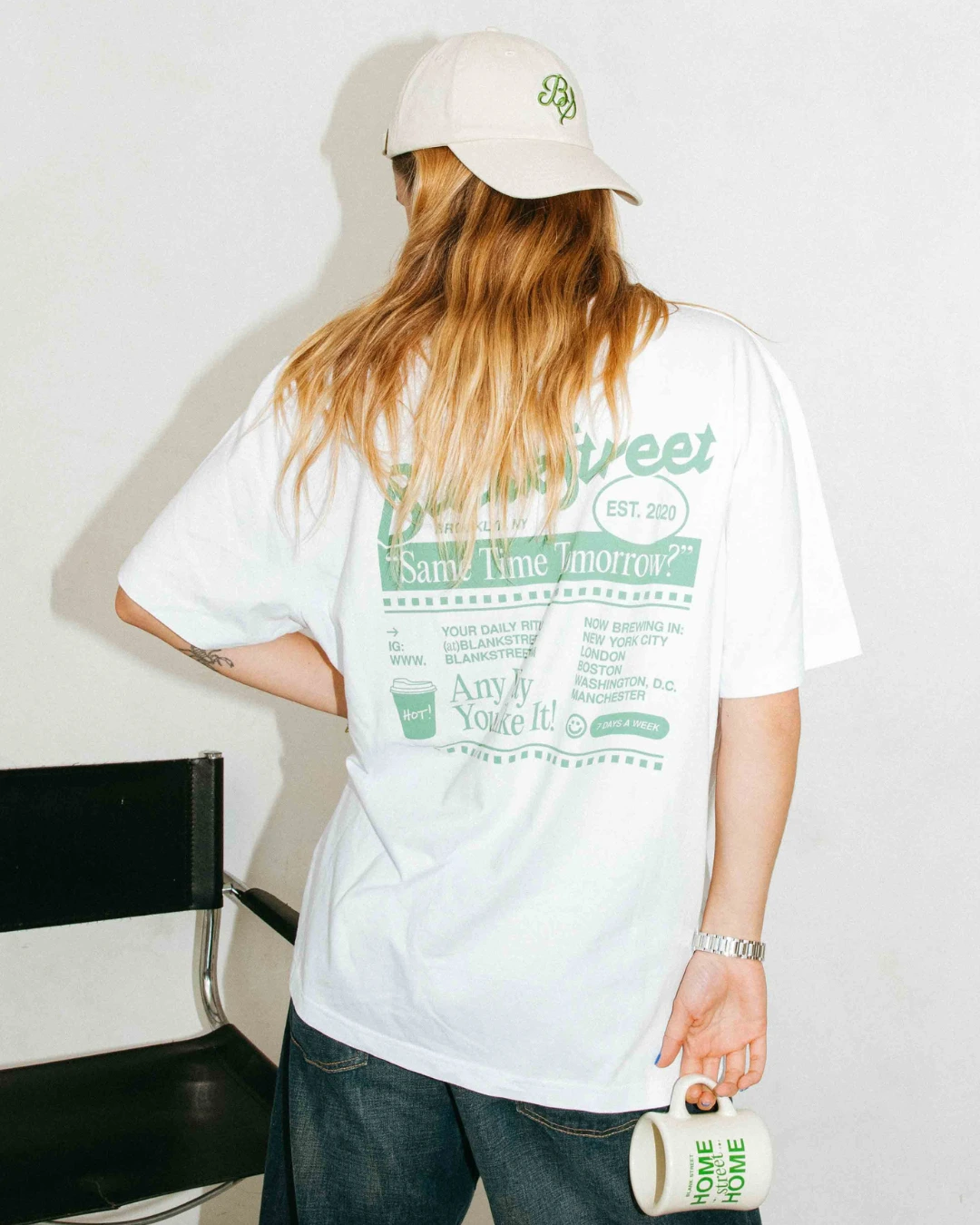Woman wearing a custom Blank Street Coffee cotton dad cap, branded graphic tee, and holding a branded ceramic mug – produced by Brand Stamp