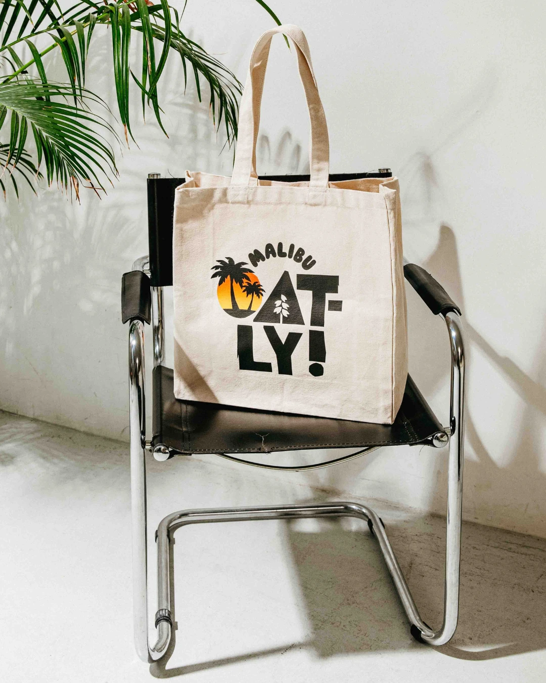 A custom large canvas tote bag made by Brand Stamp for Oatly sitting on a black arm chair